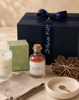 Housewarming gift box hero — New-Home Ritual kit: LOHN ORO candle, apothecary matches, linen tea towel, maple-leaf coasters and ceramic key dish in front of the navy Gitano Kit box
