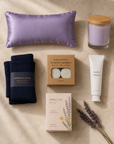 Flat-lay of Code Calm nurse recovery gift set contents on cream marble — lavender silk eye pillow, navy compression socks, eucalyptus shower steamers, hand cream, herbal tea and lavender soy candle