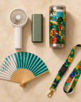 Sol & Samba flat-lay — handheld turbo fan, mini power bank, tropical tumbler, teal folding hand fan and tropical lanyard on cream marble