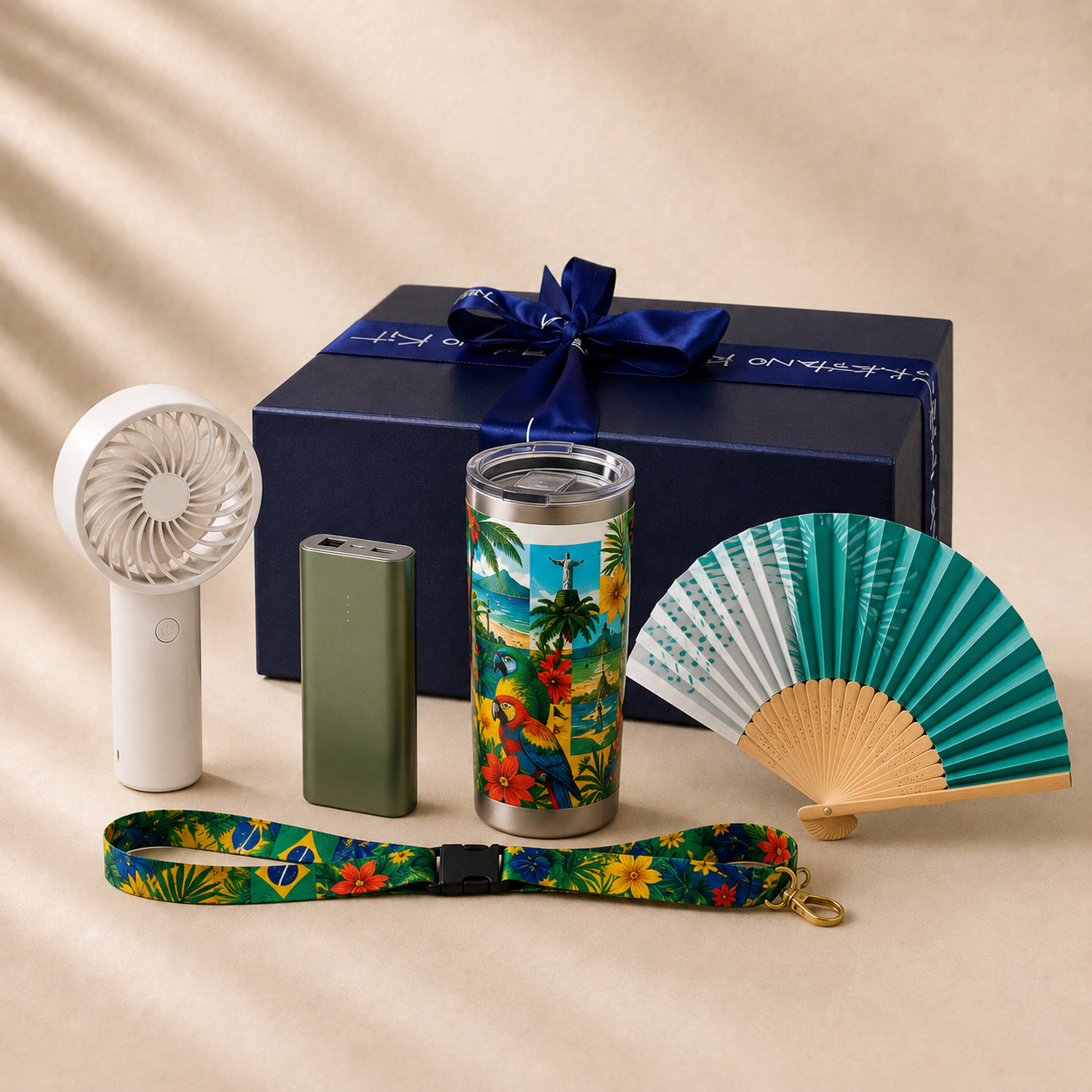Sol &amp; Samba summer stay-cool travel gift set with the real navy Gitano Kit gift box, satin ribbon, bow and silver script — handheld turbo fan, mini power bank, tropical Brazil tumbler, teal folding hand fan and lanyard on cream marble